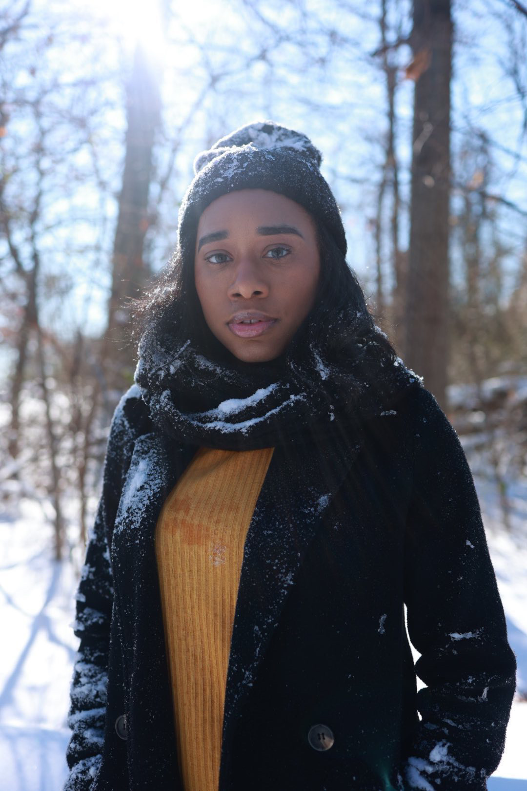 Taniya backlit by winter sun in a snow-covered black coat and scarf