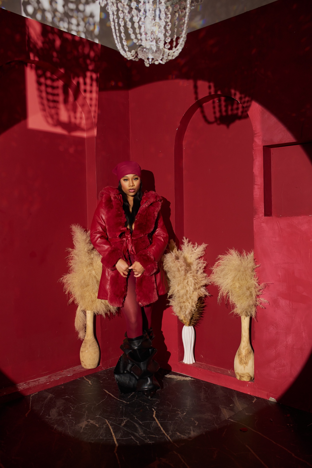 Full-length portrait of Taniya in a crimson coat beneath a chandelier and theatrical spotlight
