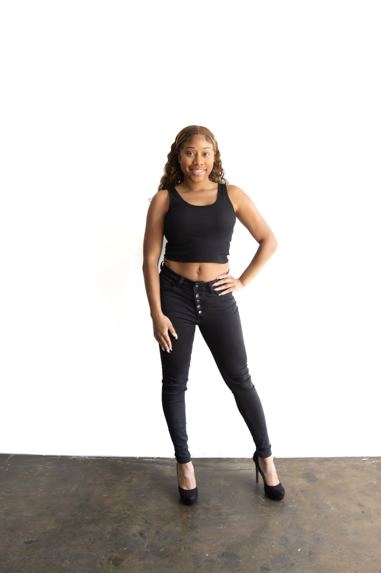 Full-length agency digital of Taniya in a black tank and black jeans against a white wall