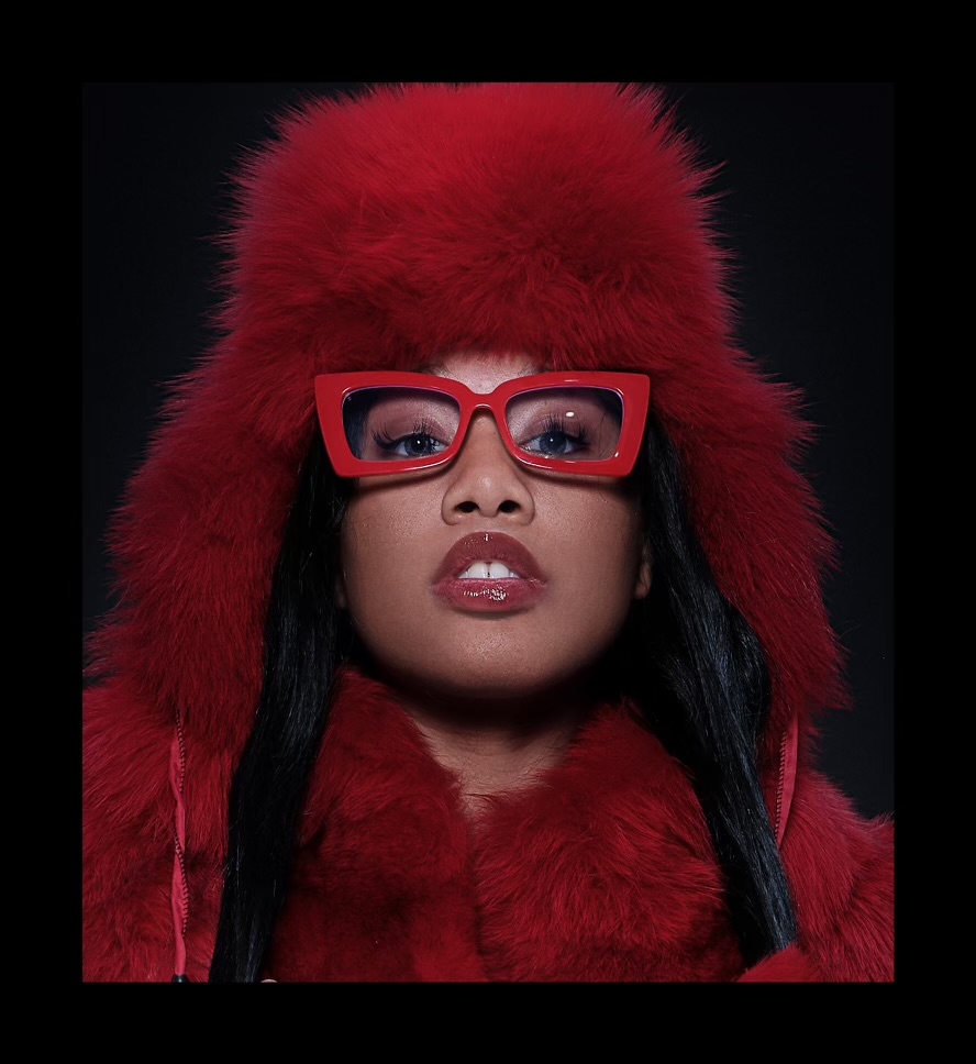 Taniya in a red fur hat, red fur coat and red rectangular sunglasses against black