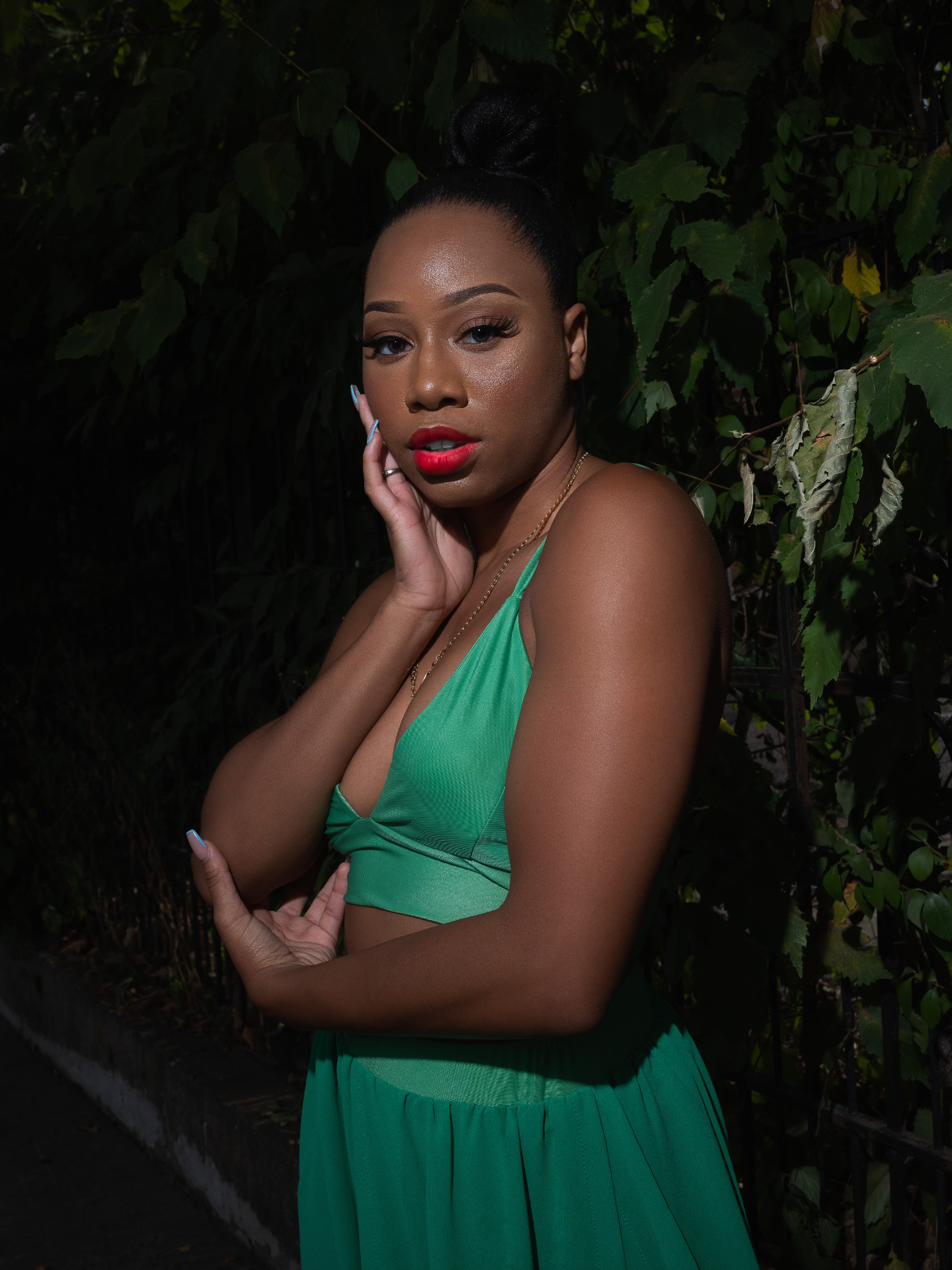 Taniya in a green dress with red lip, photographed at night against dark foliage