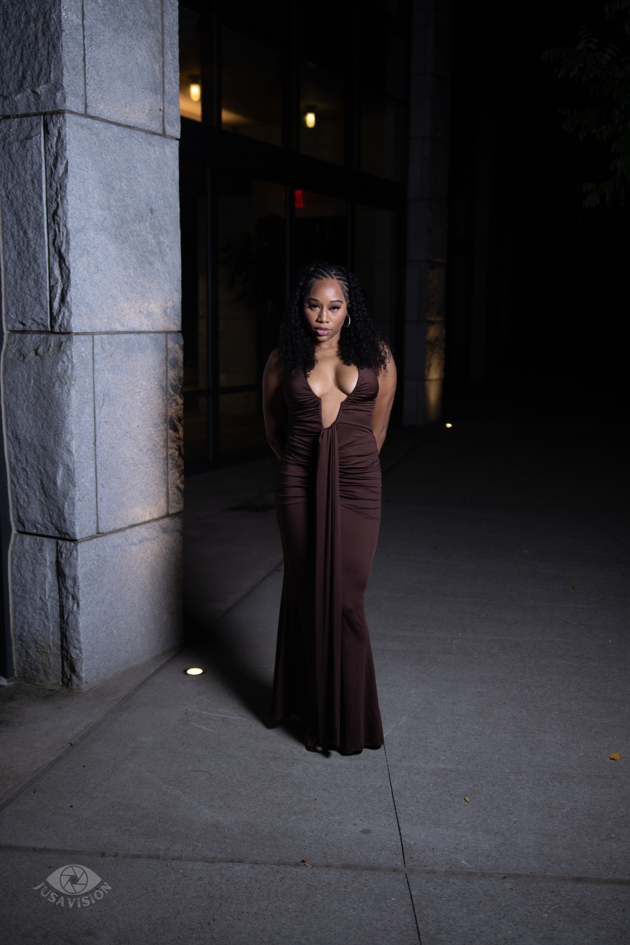 Taniya in a chocolate brown plunging evening gown outside a lit building at night