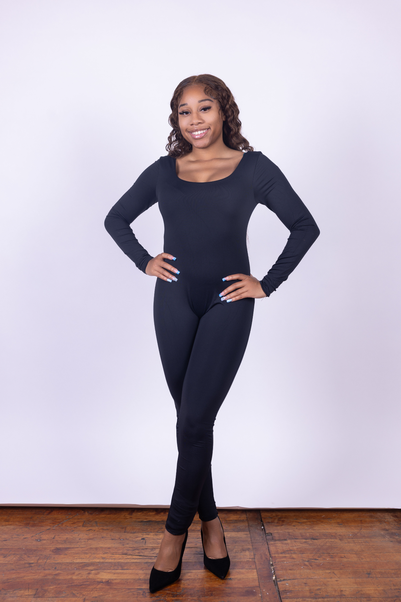 Smiling full-length digital of Taniya in a black long-sleeve unitard and heels