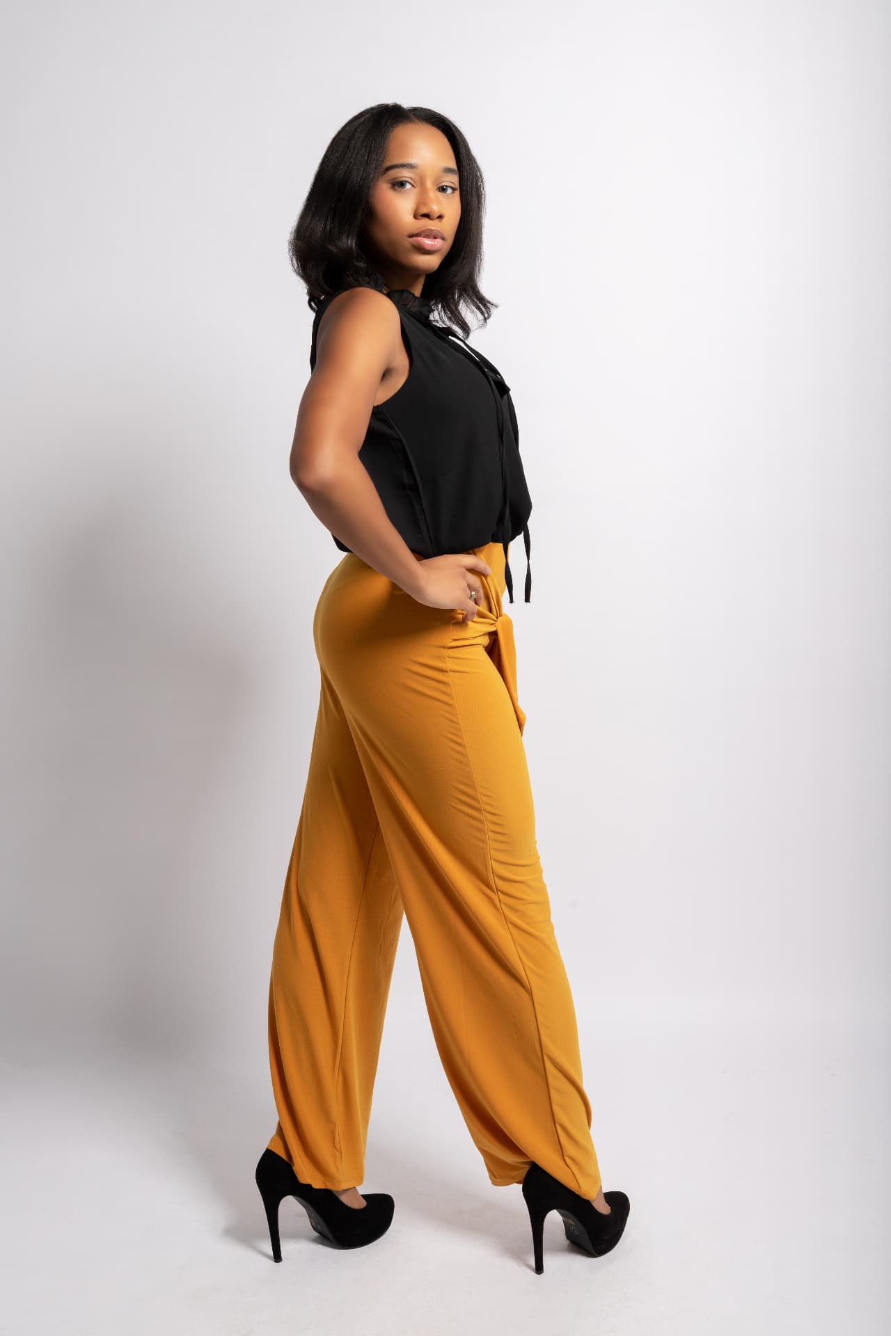 Taniya walking in profile wearing mustard wide-leg trousers and heels