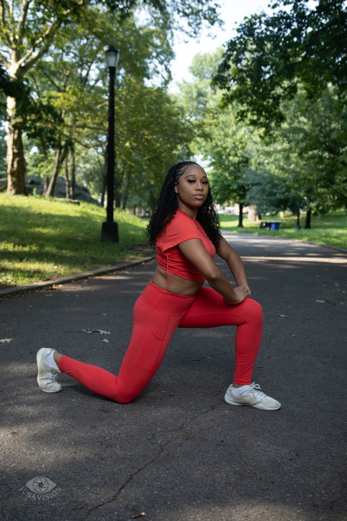 Taniya in a red crop top and leggings lunging on a sunlit park path