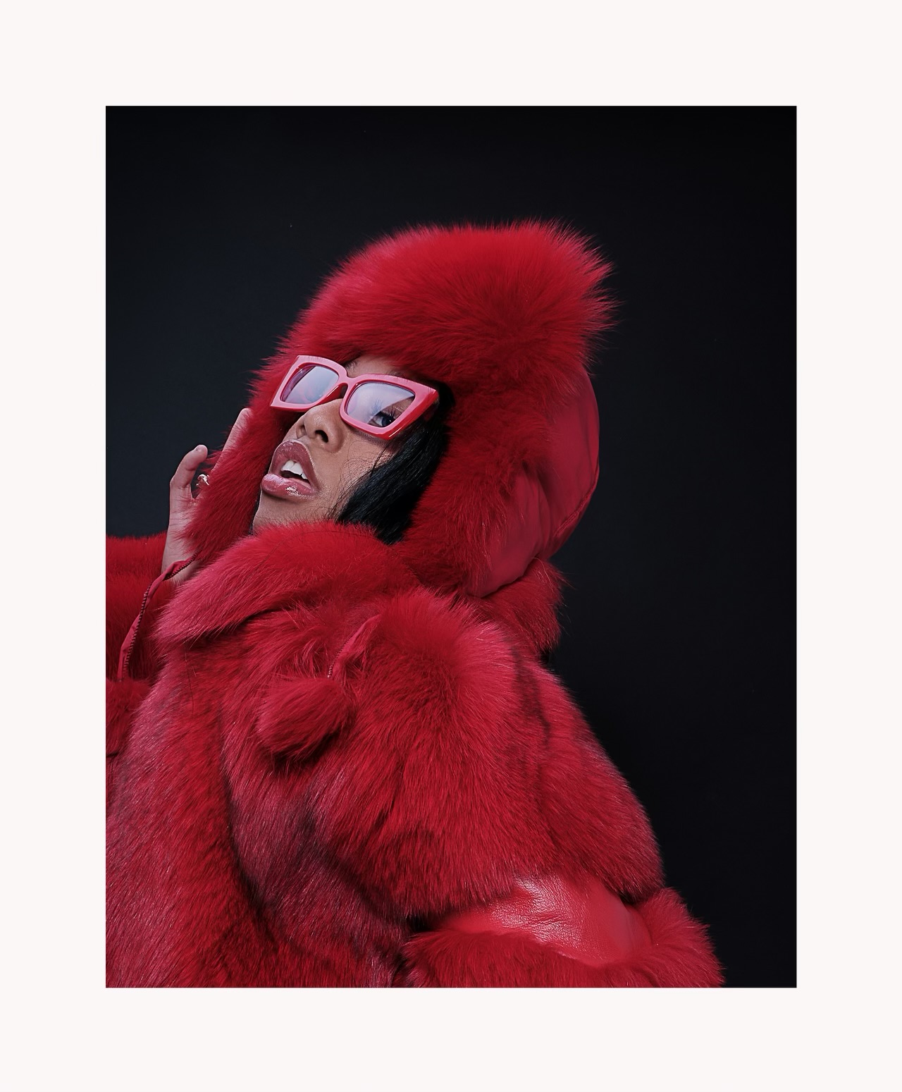Taniya in a red fur hooded coat and pink sunglasses, editorial three-quarter turn