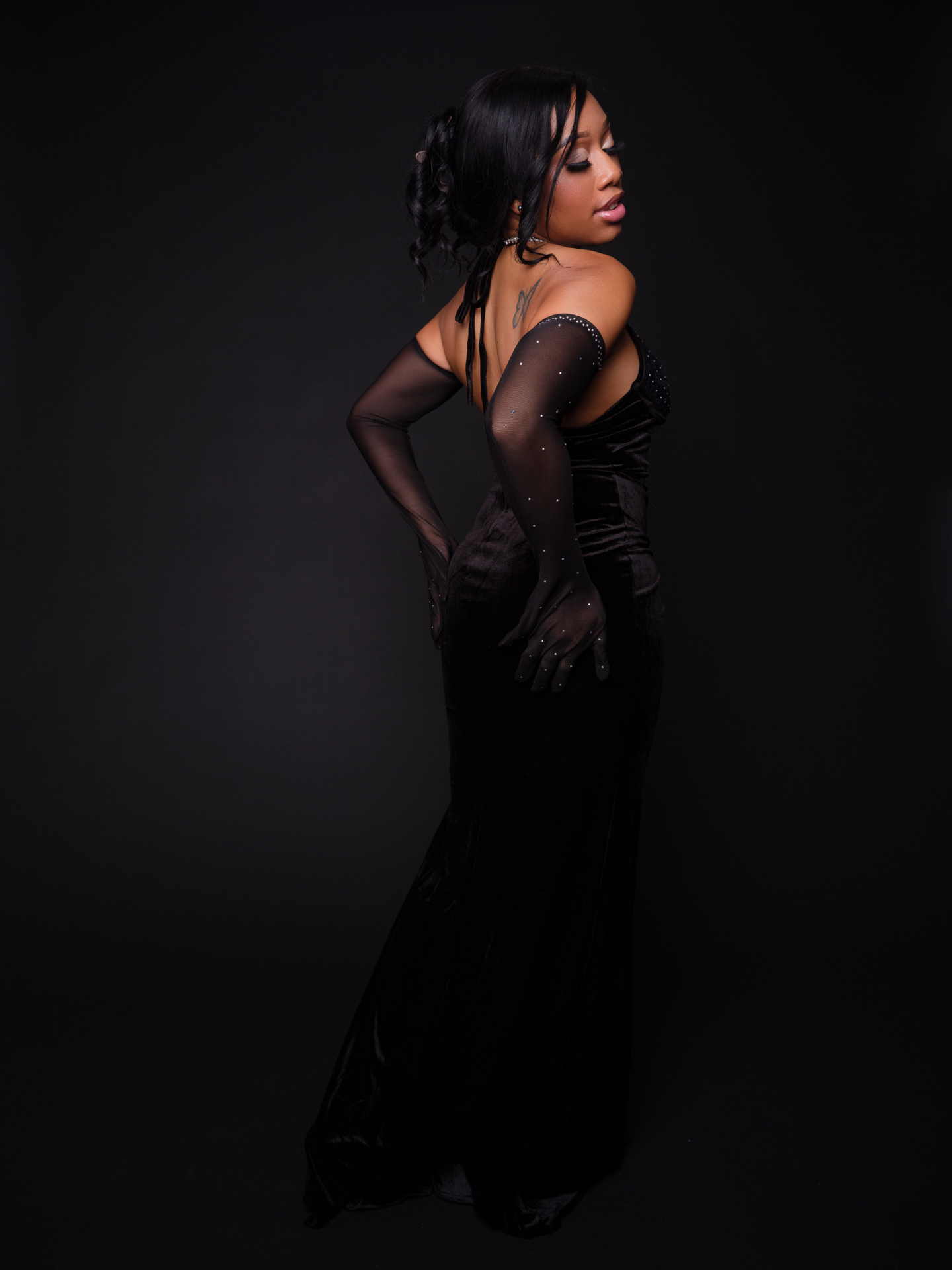 Back view of Taniya in a black velvet gown and crystal-detailed sheer gloves