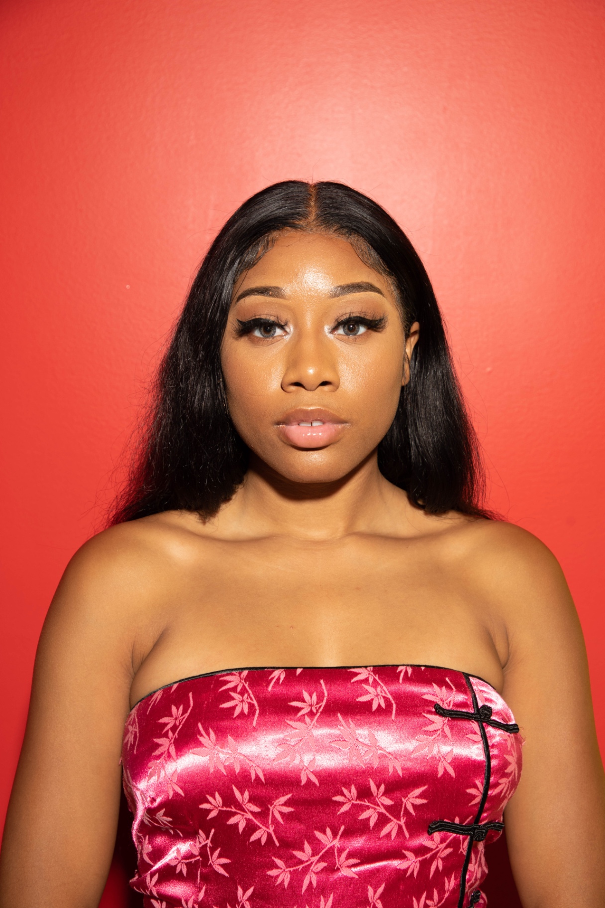 Front-facing portrait of Taniya in a pink satin brocade dress against a coral red wall