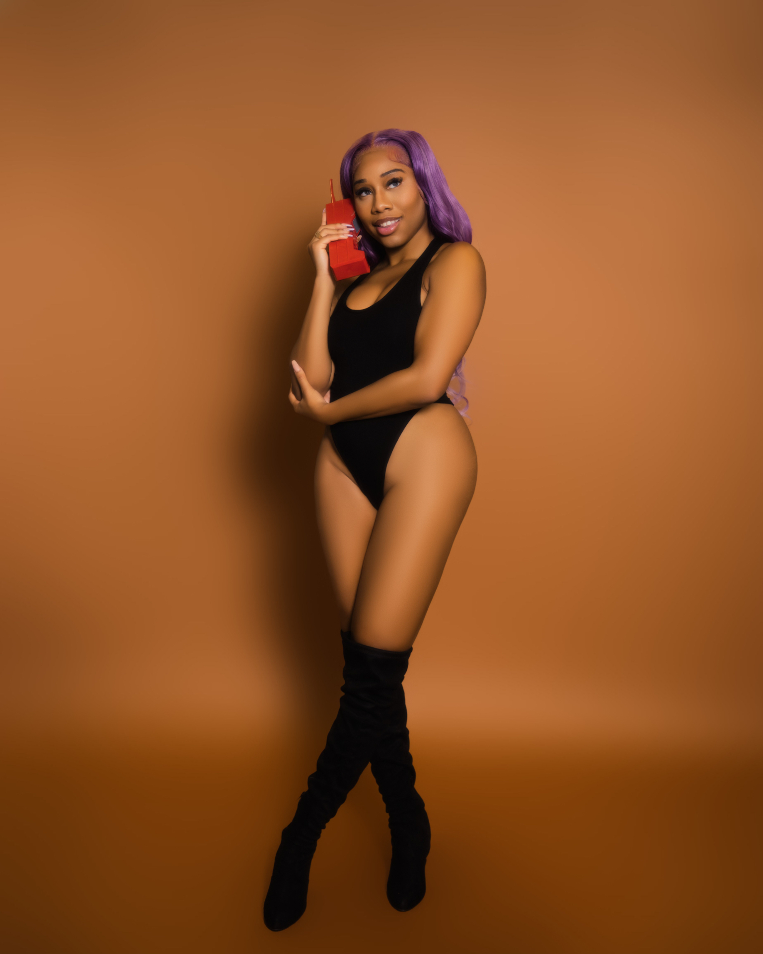 Taniya with lavender hair in a black bodysuit and thigh-high boots holding a retro red phone