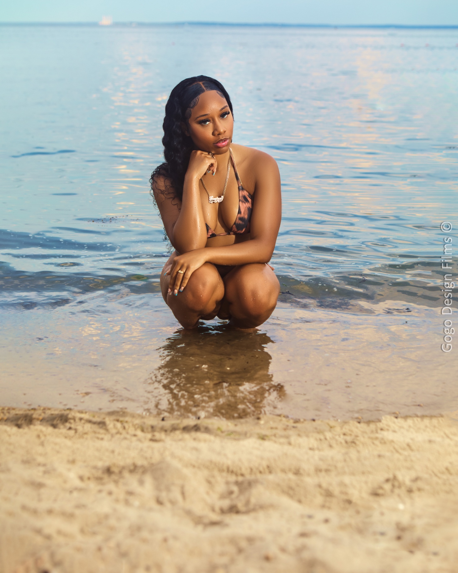 Taniya crouched in shallow water at golden hour in a leopard print two-piece