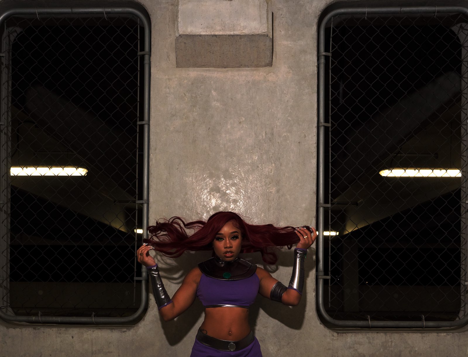 Taniya as Starfire against a concrete wall between chain-link windows, hair sweeping outward