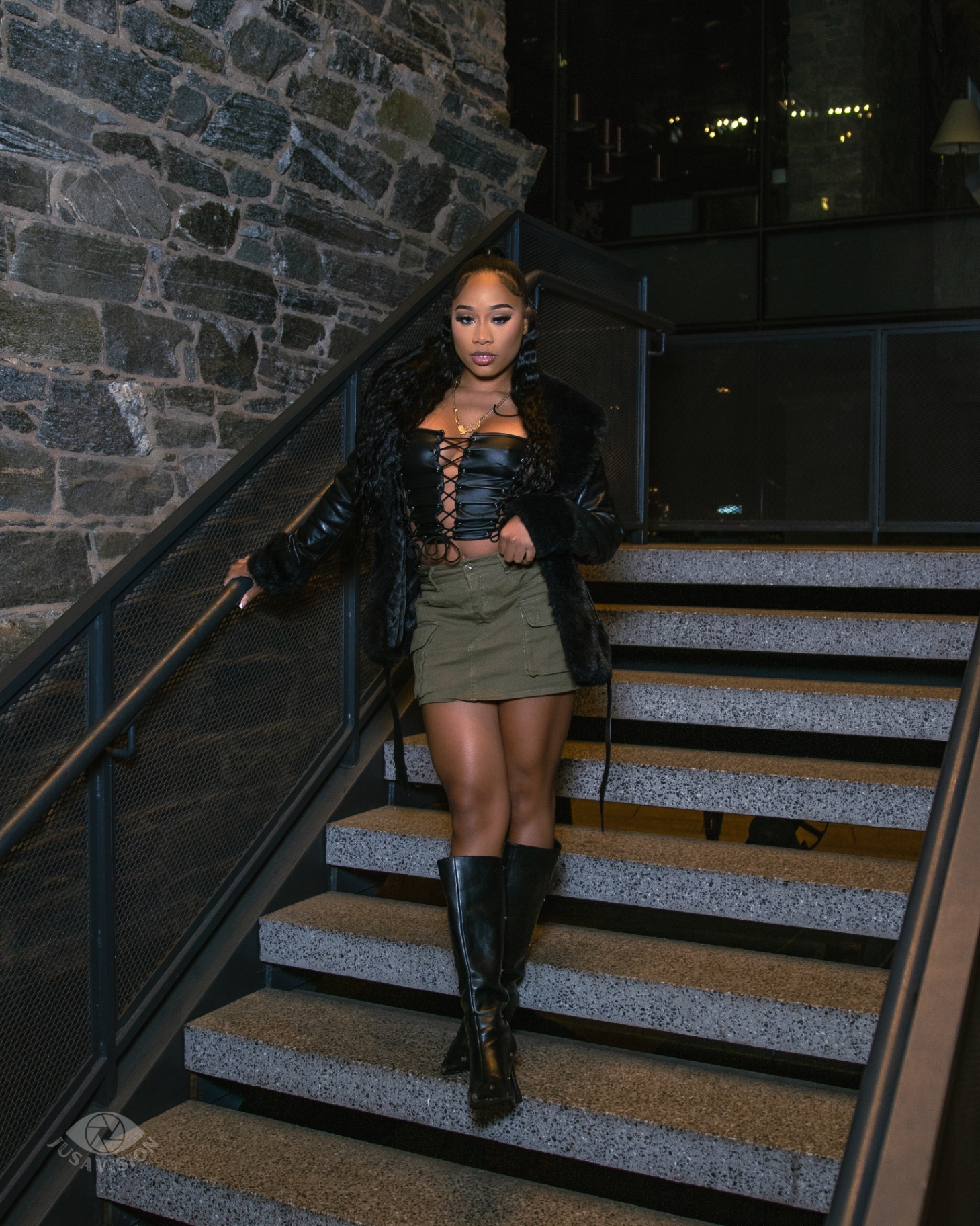 Taniya in a leather lace-up corset, fur-trim jacket and knee boots on a stone stairwell at night